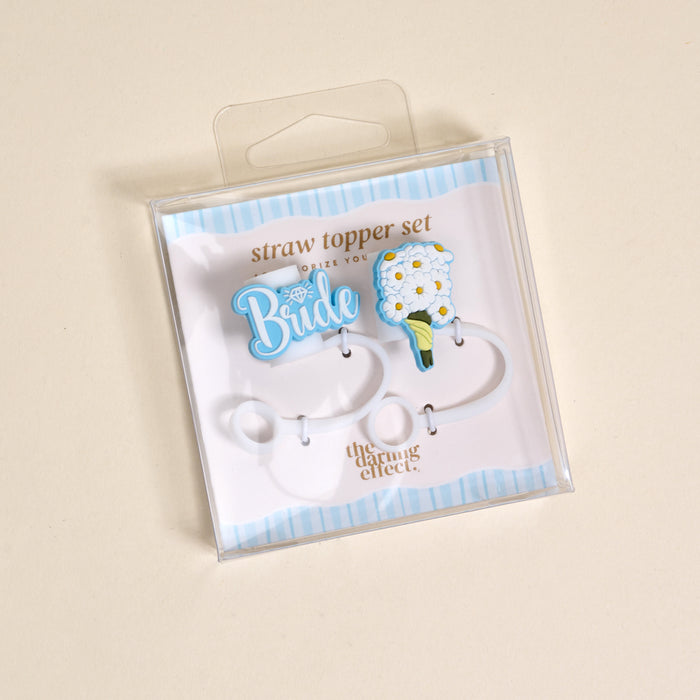 The Darling Effect's Blooming Bride Straw Topper Set includes two leak-resistant silicone toppers: a blue "Bride" with diamond and a white flower bouquet, both displayed on a chic blue and white striped background.
