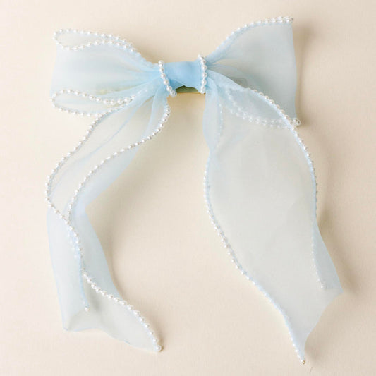 The-darling-effect Blue Sheer Pearl Hair Bow features a light blue organza bow with pearl-beaded edges, gold barrette clip, and long tails—an elegant hair accessory for any occasion. Displayed on a cream background.