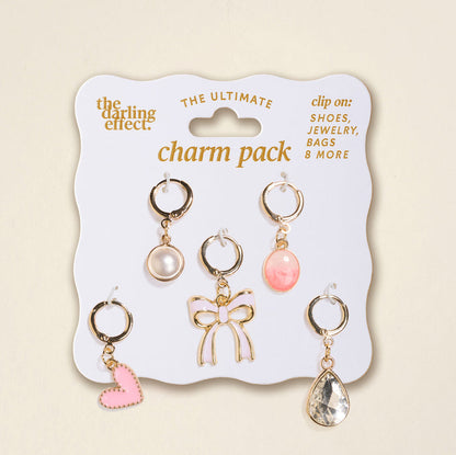 The Darling Effect’s Blush Crush The Ultimate Charm Pack includes five gold clip-on charms—a pink heart, pearl, gold bow, pink oval gem, and clear teardrop—perfect for mixing and matching with scrunchie charm sets.