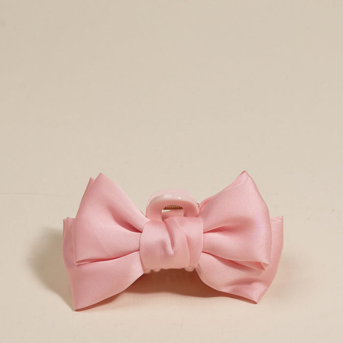 The Darling Effect's Blush Mini Satin Bow Claw Clip, featuring a pink satin bow and light pink plastic clasp, is displayed on a plain cream background.