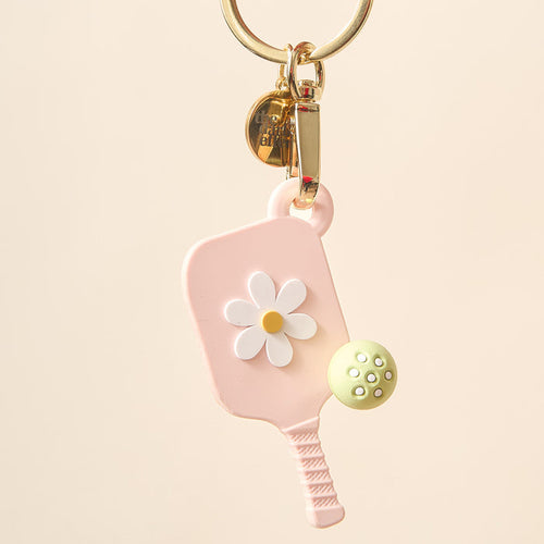 The Darling Effect's Blush Pink Pickleball Paddle Keychain features a small pink paddle with a white daisy, a green ball charm, and gold key ring—an ideal pickleball gift for fans.
