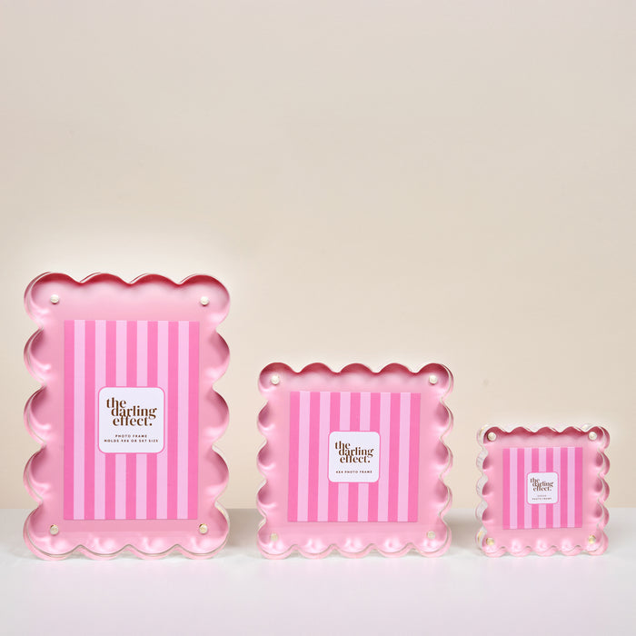 Three Blush Square Scalloped Acrylic Picture Frames by The Darling Effect are shown in small, medium, and large sizes, each with pink vertical stripes, white scallop details, and a white label for a modern, elegant look.