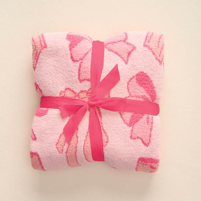 The-darling-effect Blushing Bows Pink Cozy Dreams Luxe Blanket, crafted from ultra-soft polyester microfiber with a hot pink floral pattern and satin ribbon, is shown folded on a cream background.