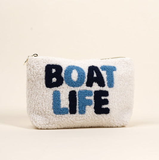 The Boat Life Teddy Pouch by the-darling-effect is a white sherpa zip pouch featuring bold blue and navy "BOAT LIFE" lettering on the front, set against a plain light background.