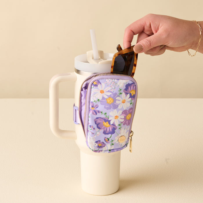 Someone puts sunglasses into the-darling-effect's Bouquet Beauty Purple Tumbler Fanny Pack, which is attached to the handle of a large white travel cup with a straw.