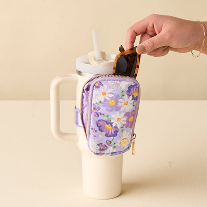 Someone puts sunglasses into the-darling-effect's Bouquet Beauty Purple Tumbler Fanny Pack, which is attached to the handle of a large white travel cup with a straw.
