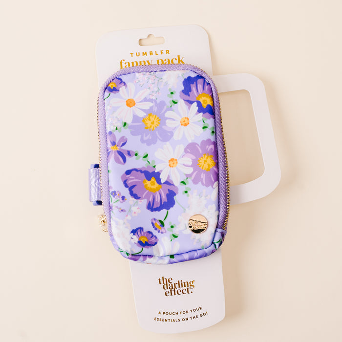 The-darling-effect’s Bouquet Beauty Purple Tumbler Fanny Pack features a stylish, water-resistant purple floral pouch with yellow, white, and purple flowers, a gold emblem, and a zipper. Displayed on cream packaging.