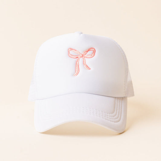 The Bow Pink Trucker Hat by the-darling-effect is a trendy white hat with a pink embroidered bow—perfect for stylish embroidered hat lovers.