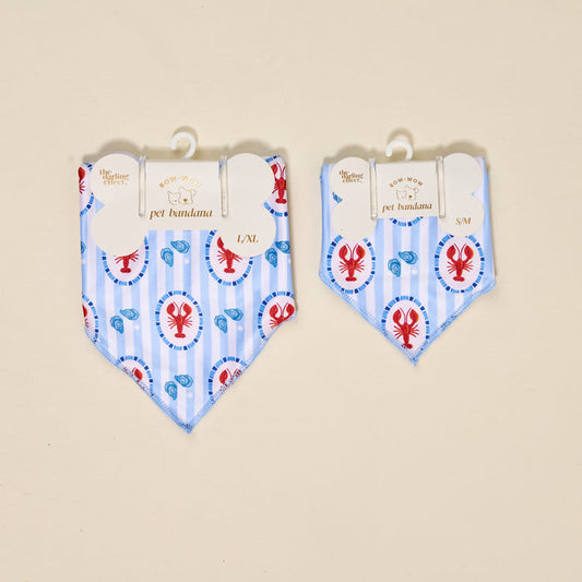 The Darling Effect Bow-Wow Pet Bandana-Harbor House, featuring blue stripes and red lobsters, is shown in L/XL and S/M sizes on hangers against a beige background—a playful accessory for your dog’s wardrobe.