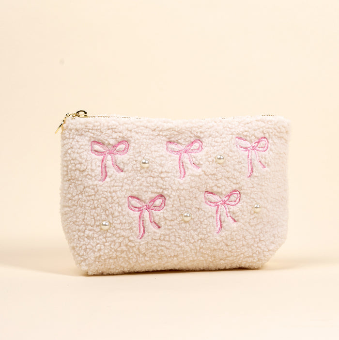 The-darling-effect’s Bows Pink Teddy Pouch is a cream sherpa zippered pouch with embroidered pink bows and pearl-like beads, shown on a beige background.