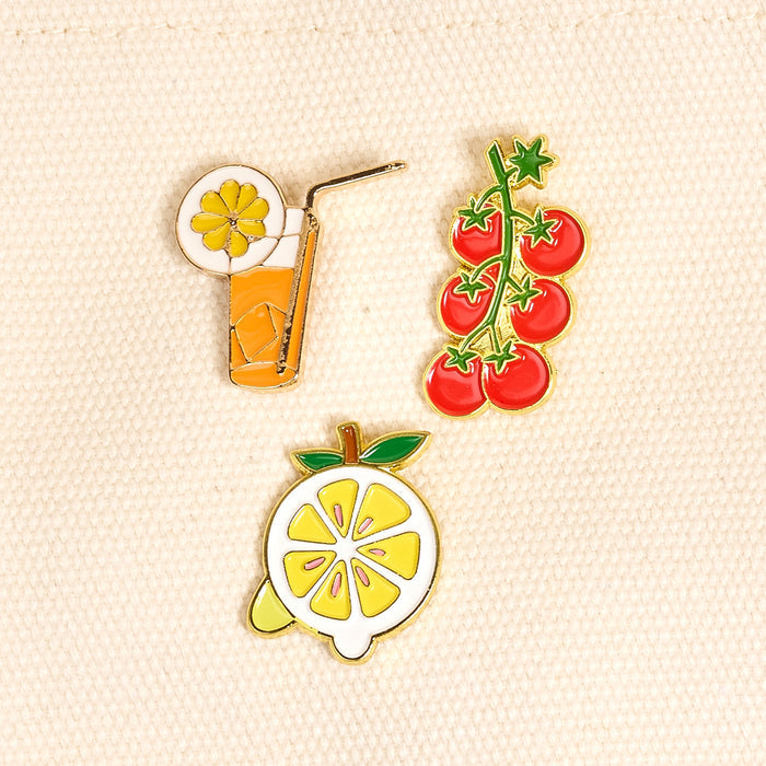 Capri Cutie The Pin Pack by The Darling Effect features three vibrant pins—a glass of orange juice, cherry tomatoes, and a lemon slice—perfect for adding playful flair to your pin collection or curated pin pack.