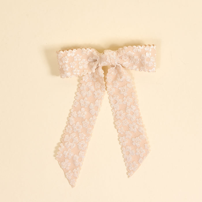 The Champagne Flower Scallop Hair Bow by the-darling-effect showcases blush pink lace with embroidered floral patterns and scalloped edges, creating a charming hair accessory displayed on a cream background.