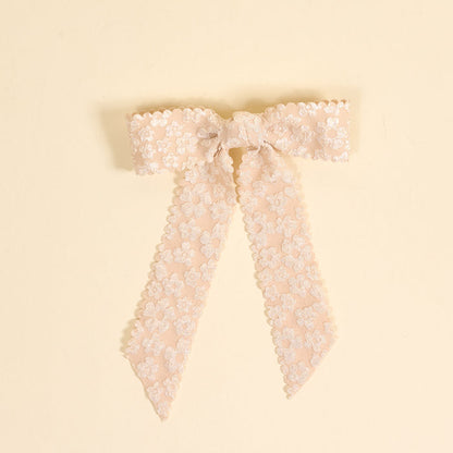 The Champagne Flower Scallop Hair Bow by the-darling-effect showcases blush pink lace with embroidered floral patterns and scalloped edges, creating a charming hair accessory displayed on a cream background.