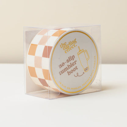 The Darling Effect Check Brown Tumbler Silicone Boot protects your tumbler in style. Displayed in a clear plastic box, its label reads "No-slip tumbler boot"—a must-have accessory for every tumbler owner.