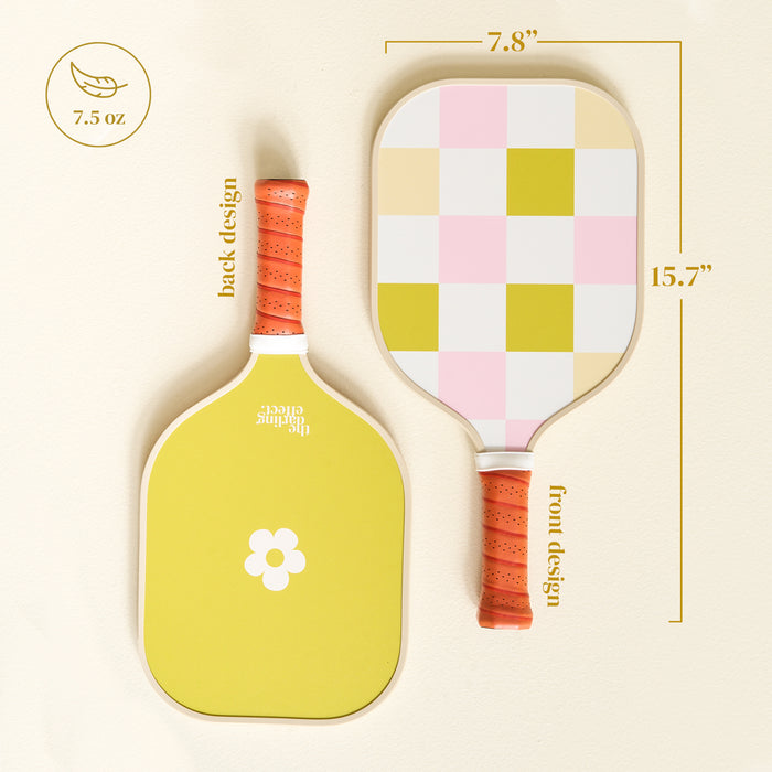 The Darling Effect’s Check Green Pickleball Paddle features orange handles, a yellow side with a white flower, a pink/yellow/white checkerboard design, and measures 7.8" x 15.7", weighing only 7.5 oz.