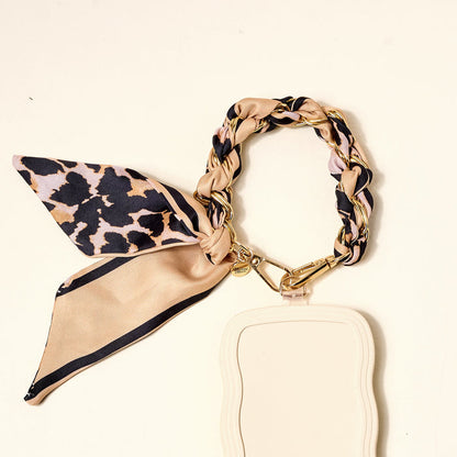 The Darling Effect's Cheetah Call Me Later Phone Scarf, featuring a beige and gold-tone chain lanyard with leopard print, is paired with a light beige badge holder—a chic accessory for everyday style.