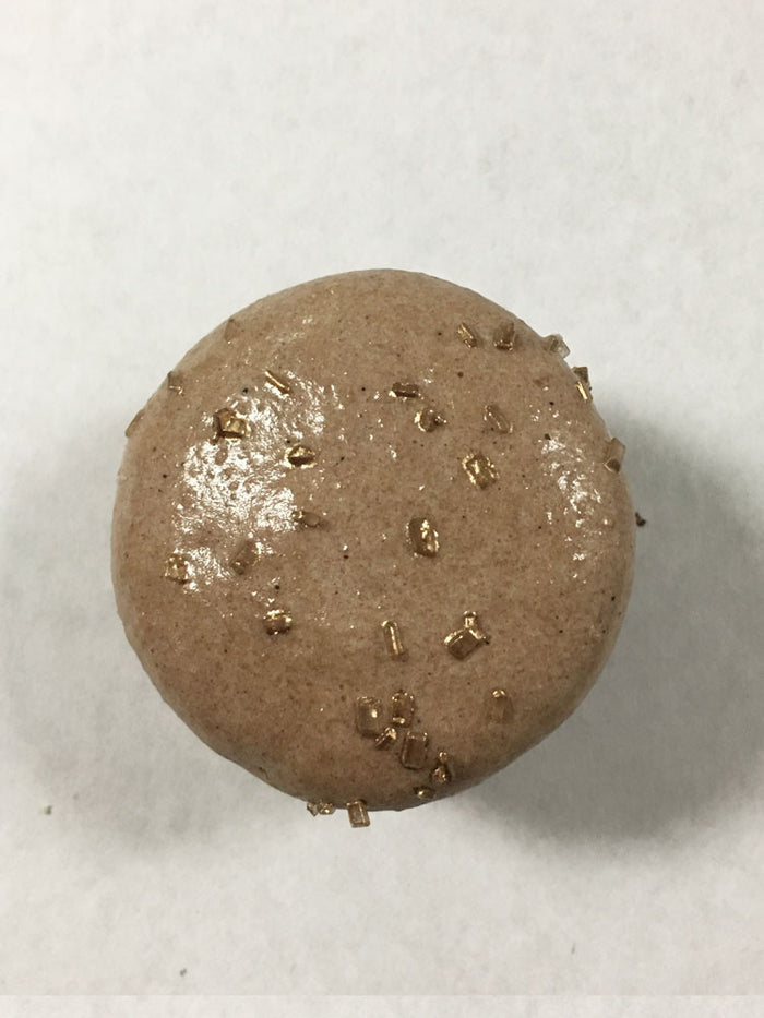 A brown chocolate macaron with gold sugar on top.