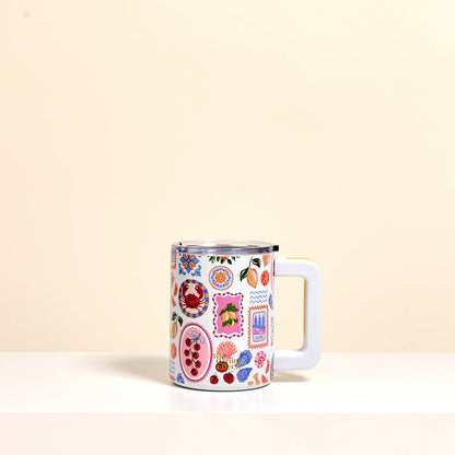 The Darling Effect’s Ciao Bella 14 oz Insulated Mug features a large handle and playful fruit, flower, and abstract designs. Its double-wall insulation keeps drinks hot or cold in style. Shown on a white surface with a beige background.