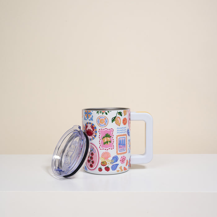 The Darling Effect’s Ciao Bella 14 oz Insulated Mug, featuring colorful floral and patterned designs, sits on a white surface. It has a clear lid and is set against a plain beige background.