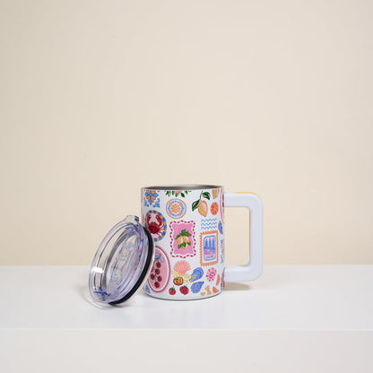The Darling Effect’s Ciao Bella 14 oz Insulated Mug, featuring colorful floral and patterned designs, sits on a white surface. It has a clear lid and is set against a plain beige background.