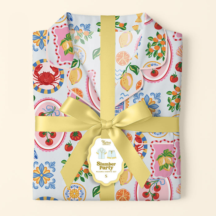 A folded Ciao Bella Slumber Party Pajama Shorts Set by The Darling Effect in ultra-soft fabric, featuring a playful print and wrapped with a yellow ribbon and tag for the ultimate relaxed fit.