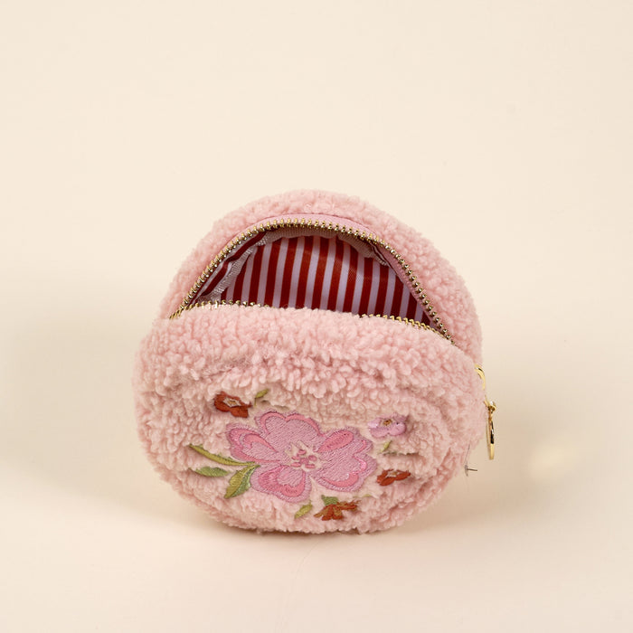 The Circle Dainty Floral Pink Teddy Pouch by the-darling-effect is a small, round, fluffy pink sherpa pouch with a zipper and embroidered flower on the front, plus red and white striped lining—perfect for your accessory set.