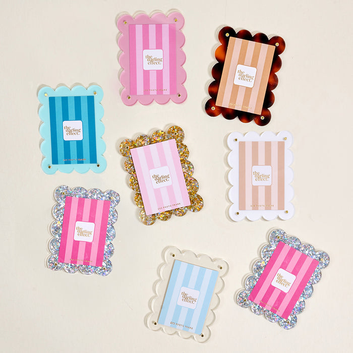 Eight colorful Clear Mini Acrylic Picture Frame Magnets by The Darling Effect, styled like mini photo frames and labeled “The Tiny Collection,” are arranged on a light background. Designs include pink, blue, gold glitter, and tortoiseshell patterns.