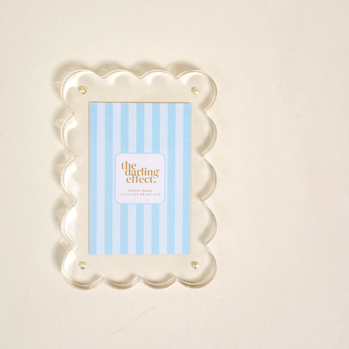 The Clear Rectangle Scalloped Acrylic Frame by the-darling-effect features scalloped edges, gold pins, and a modern design to add a chic touch to your display.