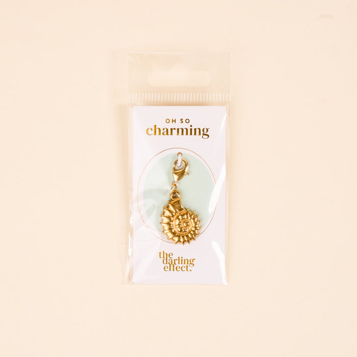 The Darling Effect's Conch Shell Jewelry Charm Gold features a clasp and comes on a white card reading "OH SO charming" and The Darling Effect, packaged in a clear bag with a light beige background—ideal for your charm bar or unique jewelry.