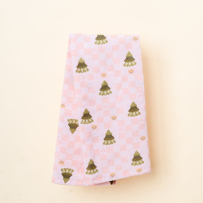 The Darling Effect's Countryside Christmas Tea Towel features a folded light pink checkered design with green trees and yellow floral motifs—ideal for festive kitchen décor, shown on an off-white background.