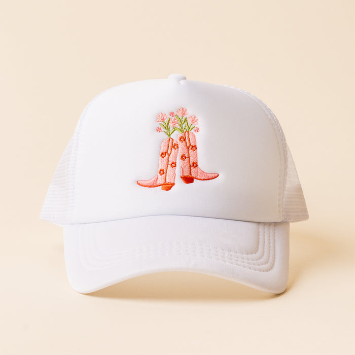 The Cowgirl Boots Trucker Hat by the-darling-effect features a trendy white mesh design with embroidered pink cowboy boots and flowers on the front, perfect for fans of unique and stylish headwear.