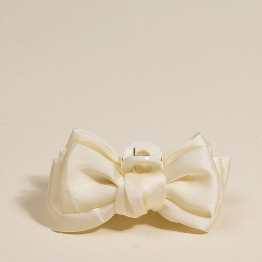 The Darling Effect’s Cream Mini Satin Bow Claw Clip features a cream-colored satin bow and sturdy plastic clasp, shown against a plain beige background.