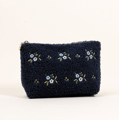 The Dainty Floral Navy Teddy Pouch by the-darling-effect features textured sherpa fabric, small embroidered light blue flowers, and a zipper, shown against a plain light background.