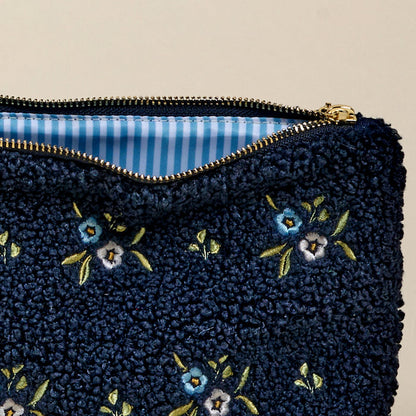 The-darling-effect's Dainty Floral Navy Teddy Pouch features blue and white embroidered flowers, a gold zipper, and a striped interior—an ideal accessory for your collection.