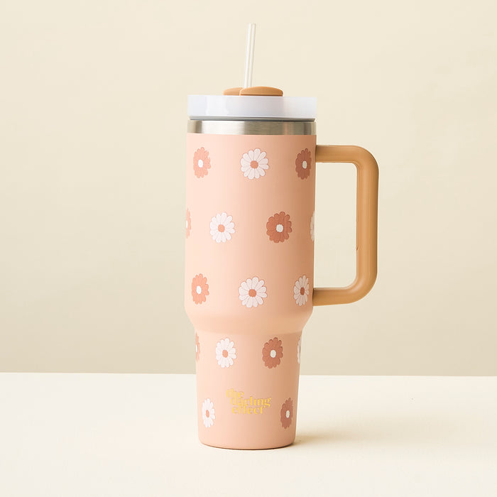 The Darling Effect Darling Daisy Tan 40 oz Take Me Everywhere Tumbler features a large handle, clear lid, straw, and peach daisy-like flower design. It sits on a light surface against a beige background.