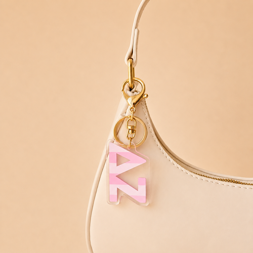 A cream-colored handbag with a gold keychain on the strap, featuring The Darling Effect’s Delta Zeta Stripes Acrylic Keychain—perfect as a chic sorority gift or bid day accessory against a beige background.