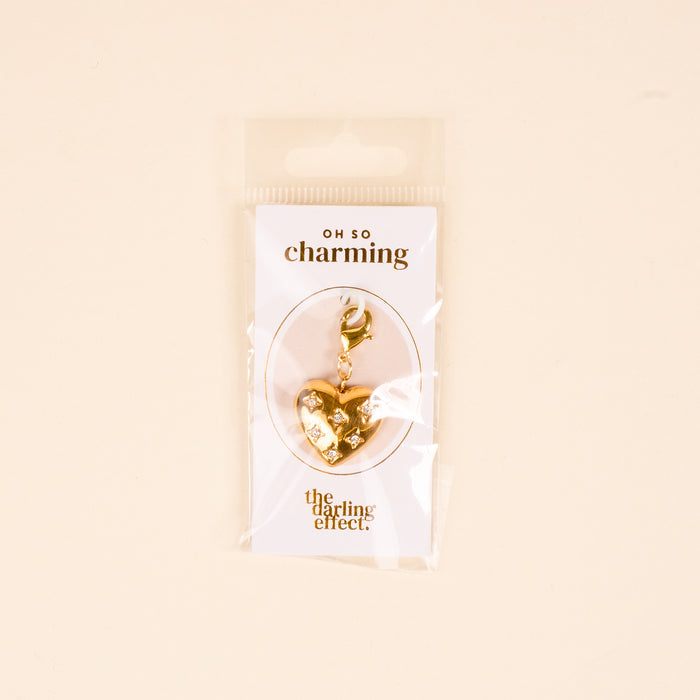 The Diamond Heart Jewelry Charm Gold by The Darling Effect features a gold, heart-shaped design with a clasp, packaged on an "OH SO charming" card—perfect for adding a meaningful touch to your charm bar.