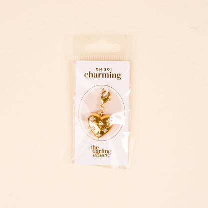 The Diamond Heart Jewelry Charm Gold by The Darling Effect features a gold, heart-shaped design with a clasp, packaged on an "OH SO charming" card—perfect for adding a meaningful touch to your charm bar.