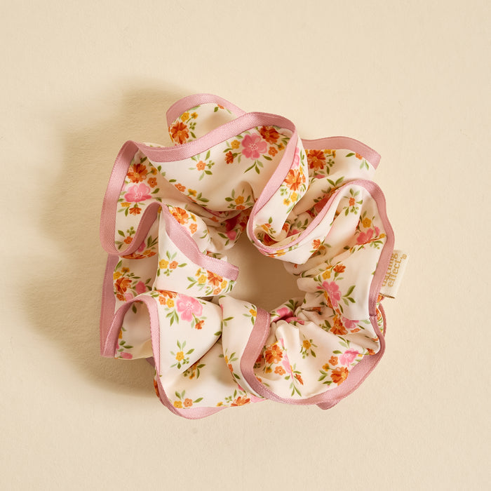 The Darling Effect's Endless Daydream Cream Ruffle Up Scrunchie features oversized ruffles, pink-edged cream fabric, and a floral print with pink and orange flowers—an elegant hair accessory perfect for any occasion.