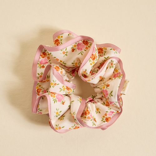 The Darling Effect's Endless Daydream Cream Ruffle Up Scrunchie features oversized ruffles, pink-edged cream fabric, and a floral print with pink and orange flowers—an elegant hair accessory perfect for any occasion.