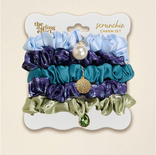 The Darling Effect's Endless Daydream Navy Scrunchie Charm Set features five stylish scrunchies in light blue, dark blue floral, teal, and olive green, each adorned with a unique charm like a pearl, gold disc, or green gem.