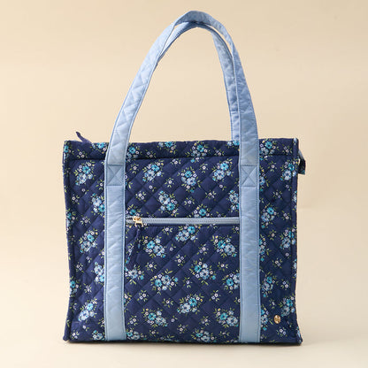 The-darling-effect’s Endless Daydream Navy The Everyday Quilted Tote Bag features a blue floral pattern, light blue handles, and a front zippered pocket—perfect for daily style and convenience, shown against a plain beige background.