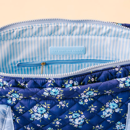 A close-up of the Endless Daydream Navy The Everyday Quilted Tote Bag by the-darling-effect, with blue floral print, light blue and white striped lining, a small zip pocket, and THE DARLING EFFECT label—ideal for daily use.