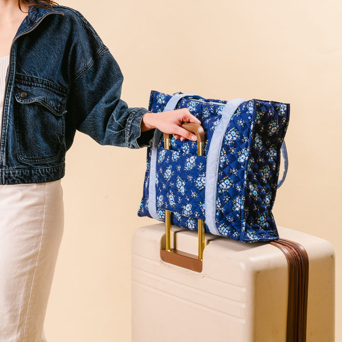 A woman in a denim jacket holds the-darling-effect's Endless Daydream Navy The Everyday Quilted Tote Bag, standing beside a light-colored suitcase.
