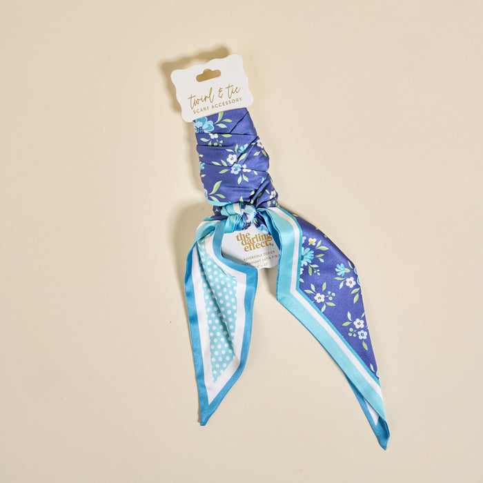 The Darling Effect's Endless Daydream Navy Twirl & Tie Scarf Accessory features blue floral fabric with polka dot trim, packaged on a white card. Style it endlessly for a versatile look.