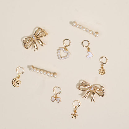 The Fancy Flair Dazzle Shoe Charm Pack by the-darling-effect features gold and pearl bows, hearts, a crescent moon, star, flower, and pearl-accented charms—ideal for elegant hairstyles or as unique shoe charms. Arranged on a light beige background.
