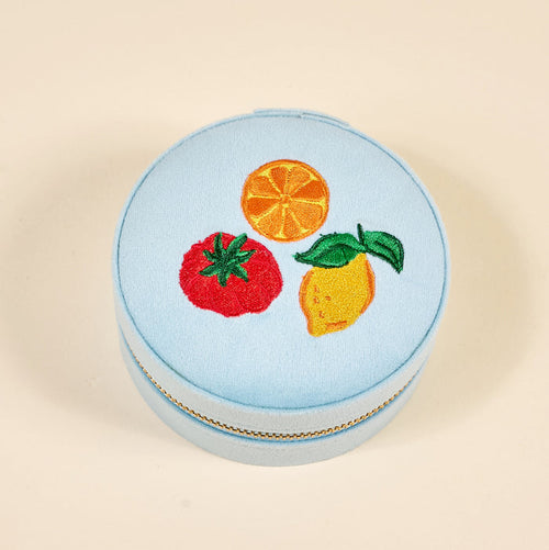 The Darling Effect Fruit Market Round Velvet Jewelry Case is a light blue, gold-zippered box with embroidered orange, lemon, and tomato designs—an ideal travel organizer for your favorite accessories.