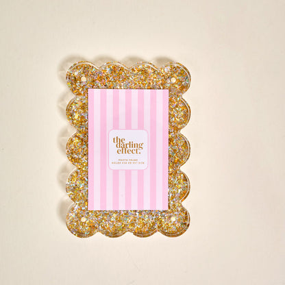 The Darling Effect Gold Glitter Rectangle Scalloped Acrylic Picture Frame is shown vertically on a cream background with a pink and white striped insert reading "the darling effect.