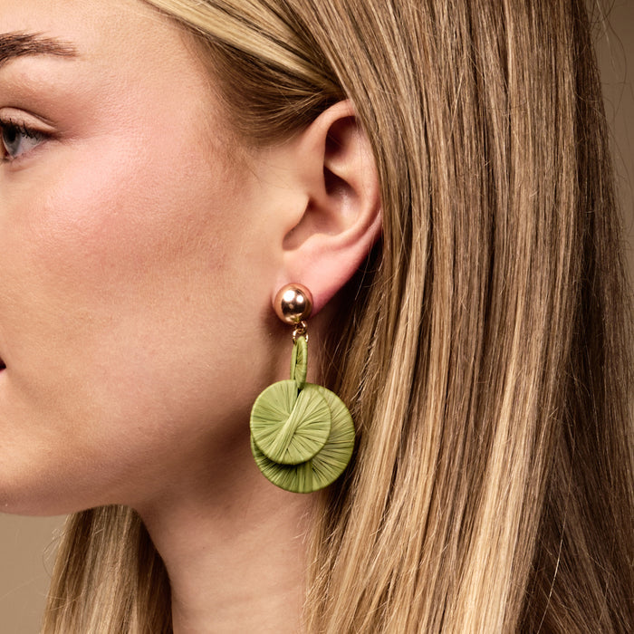 A woman's ear is adorned with The Darling Effect's Green Pretty and Polished Earrings—lightweight, layered, light green raffia earrings that add effortless boho style to any everyday look.