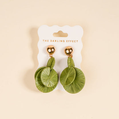 Green Pretty and Polished Earrings by The Darling Effect feature round green leaf-patterned designs with gold studs—ideal for elevating your everyday style. Shown on a white card against a beige background.